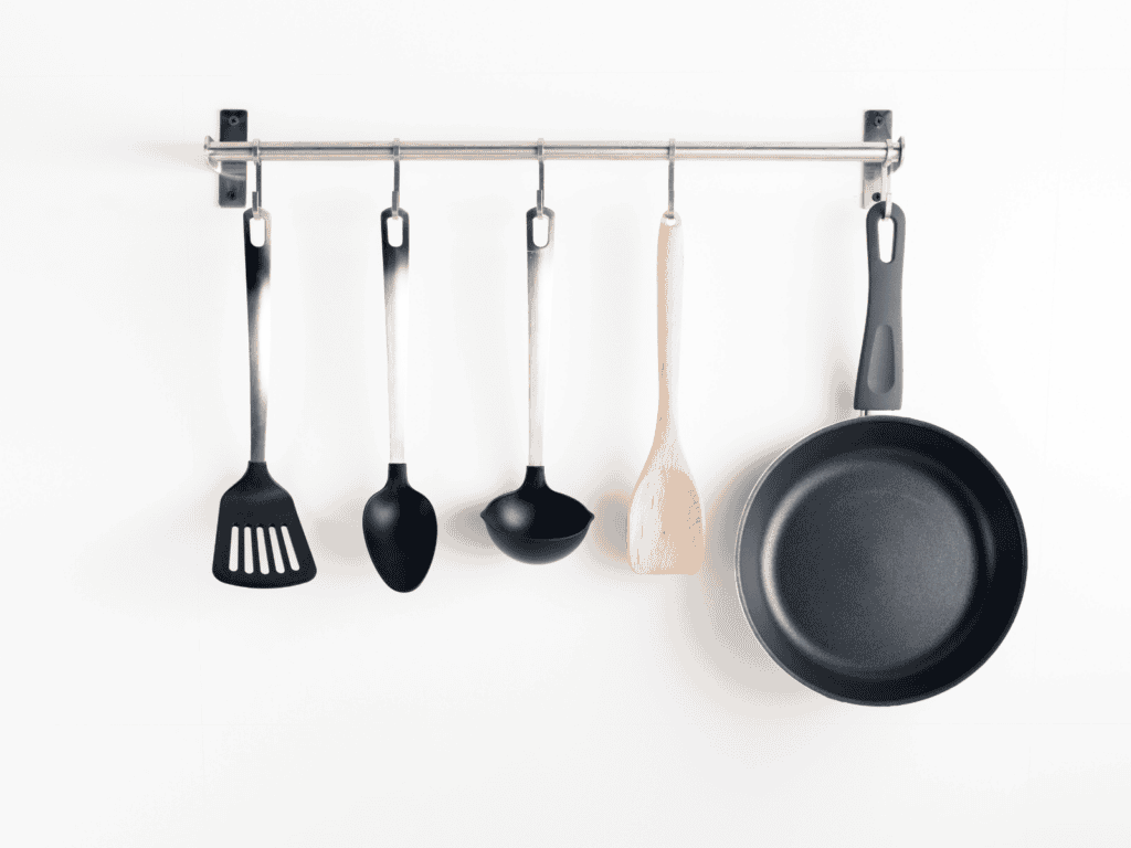 A rack mounted to a door and a pan and cooking utensils are hanging from it.