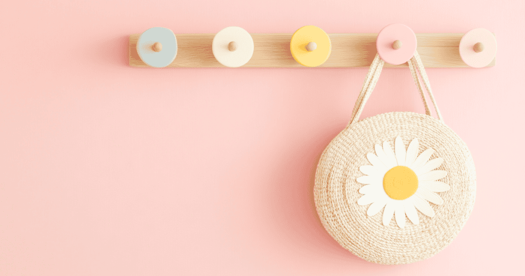 Pink wall with multi colored hooks and a small purse with a flower hanging on a hook