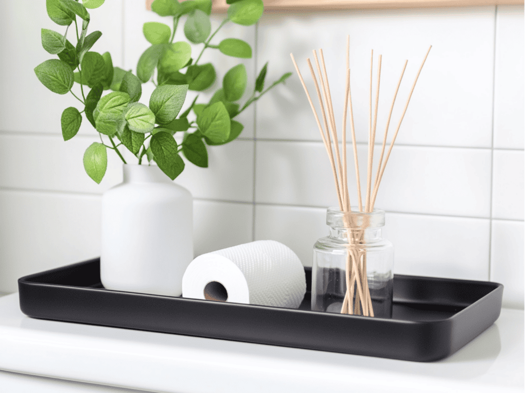 Black tray on the back of a toilet that has a plant and a roll of toilet paper on it