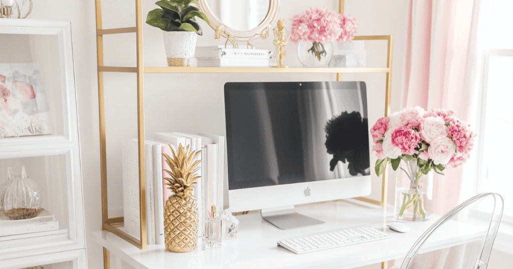 White desk with pink accessories and books beside the computer