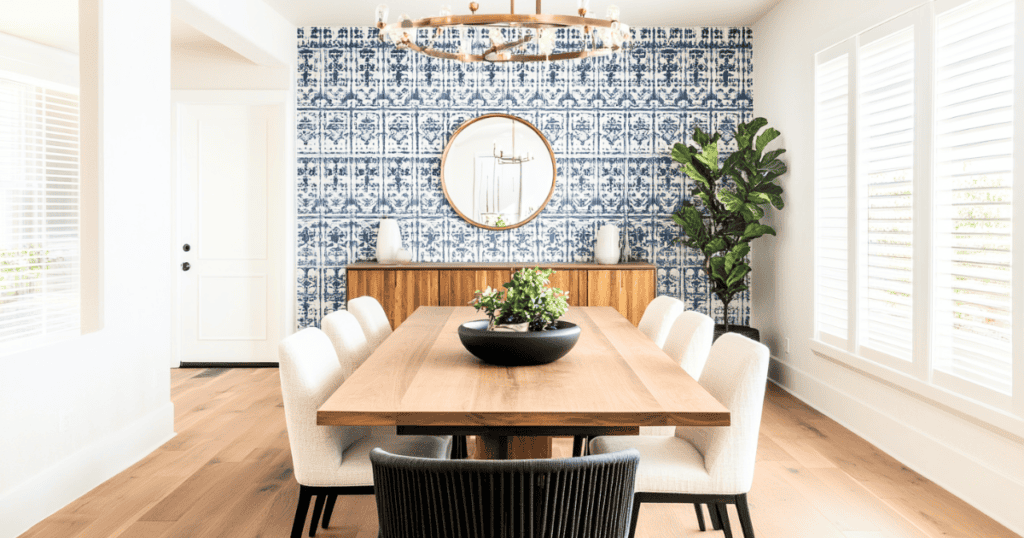 Wooden dining room table with white chairs. An accent wall with blue wallpaper.