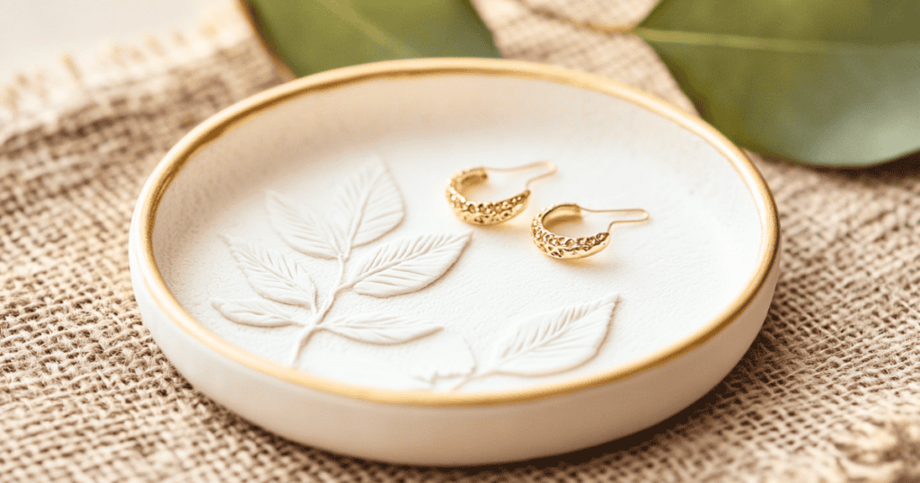 Small round white dish trimmed in gold with a pair of gold earings inside