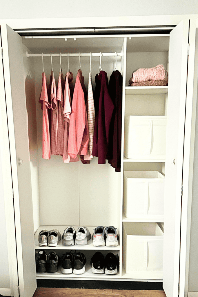 Pastel colored clothes hanging in a white closet with shelves on the side and a shoe rack on the bottom