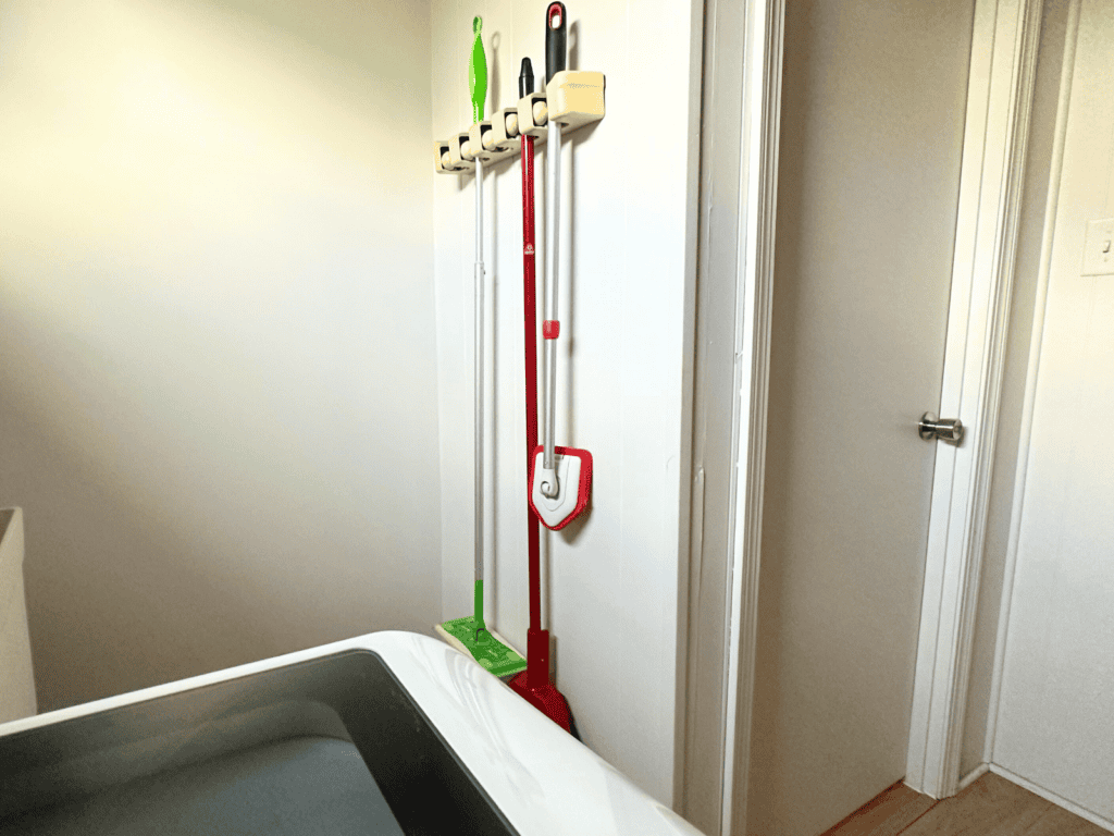 Mop and broom hanging on a small wall in a laundry room