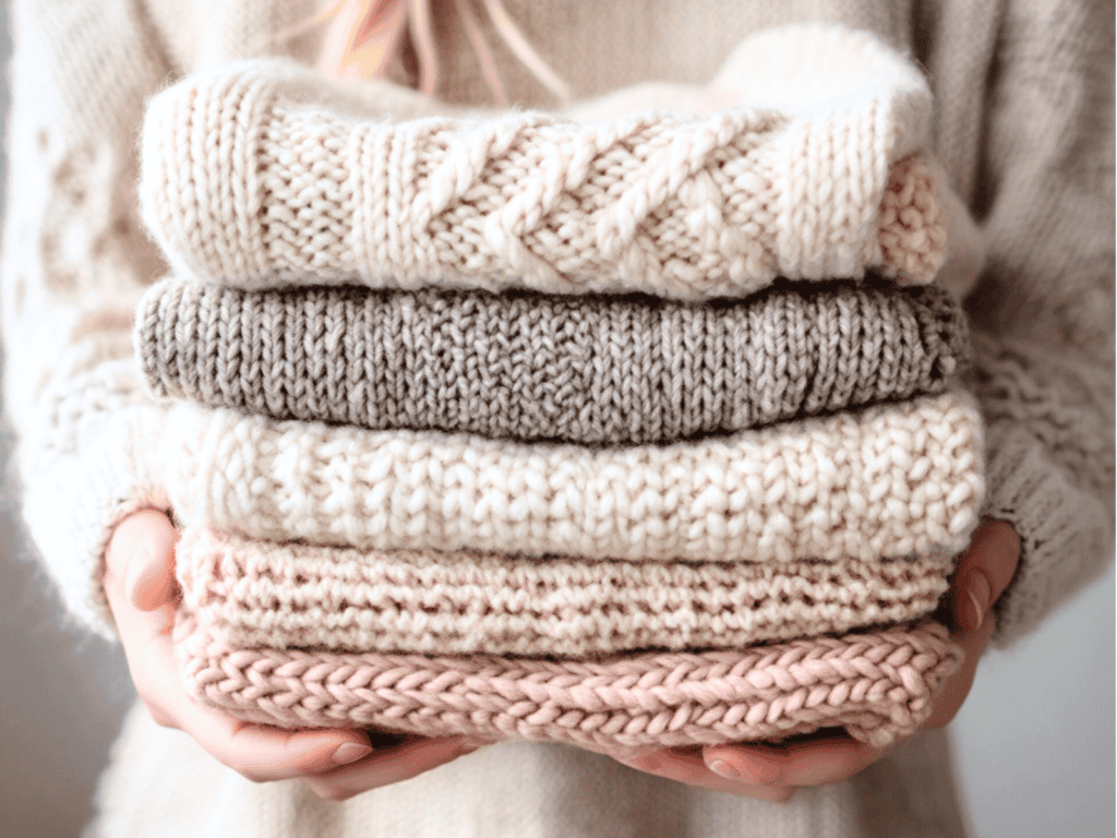 A woman holding a stack of sweaters