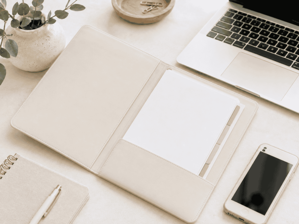 Folder of papers on a desk beside a phone and a computer.
