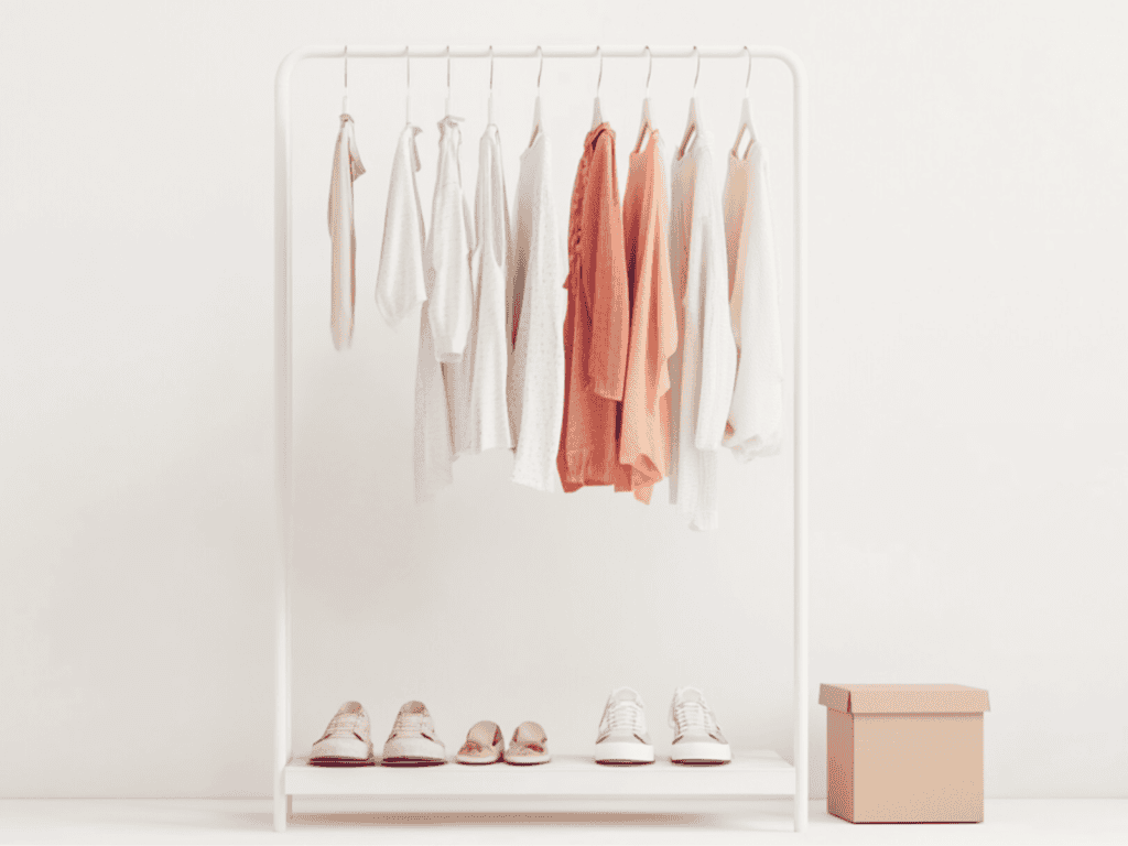 Clothes rack with clothes hanging from it and shoes below and a box beside of it