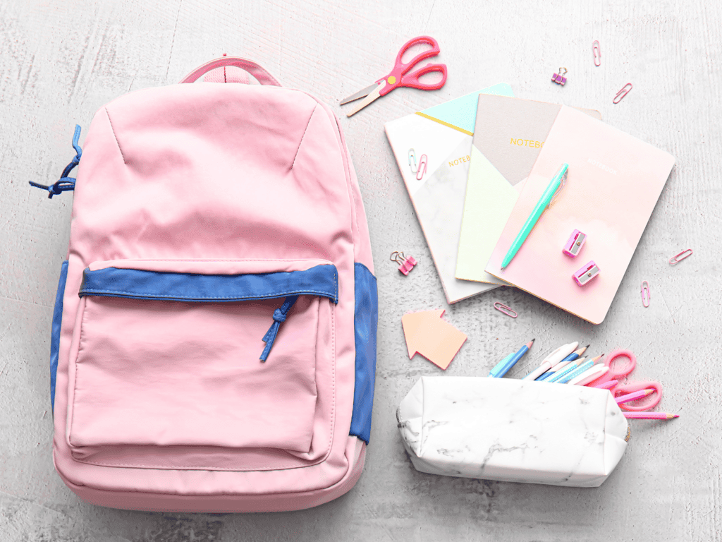 Pink backpack with papers, scissors, and a pencil box laying beside it.