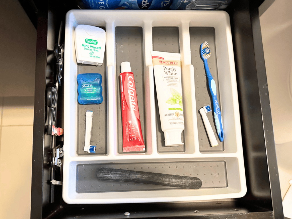 A silverware tray in a bathroom drawer that contains toothbrushes, dental floss, and toothpaste.