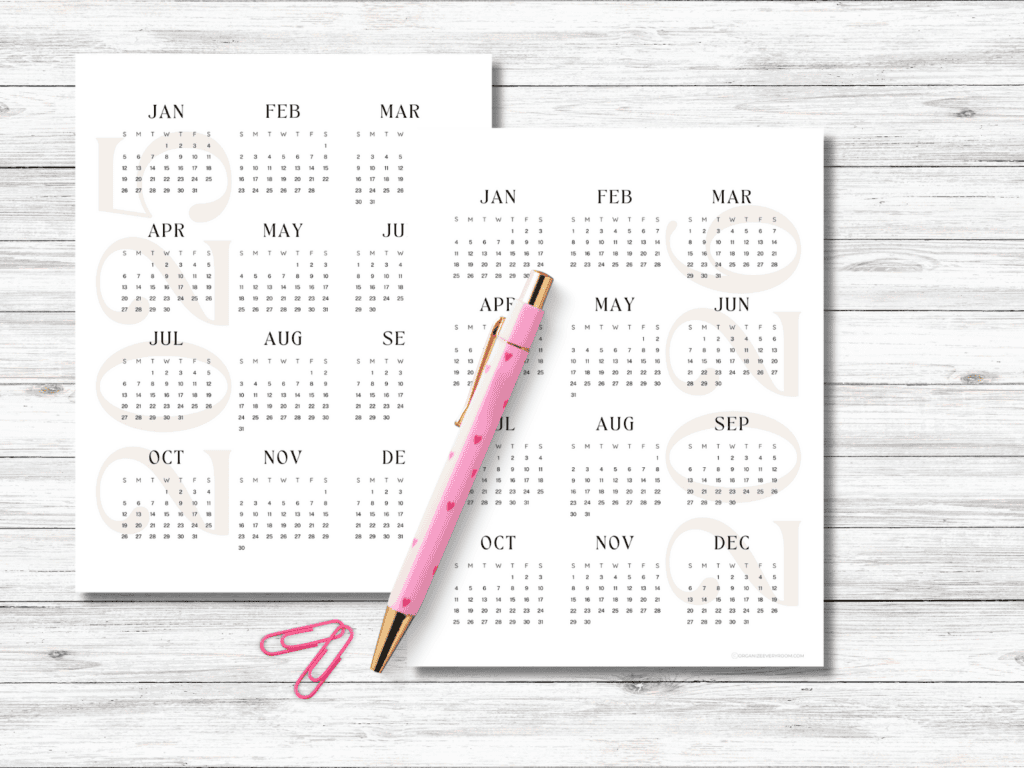 The year 2025 and 2026 calendar pages on a desk with a pink pen and pink paper clips.