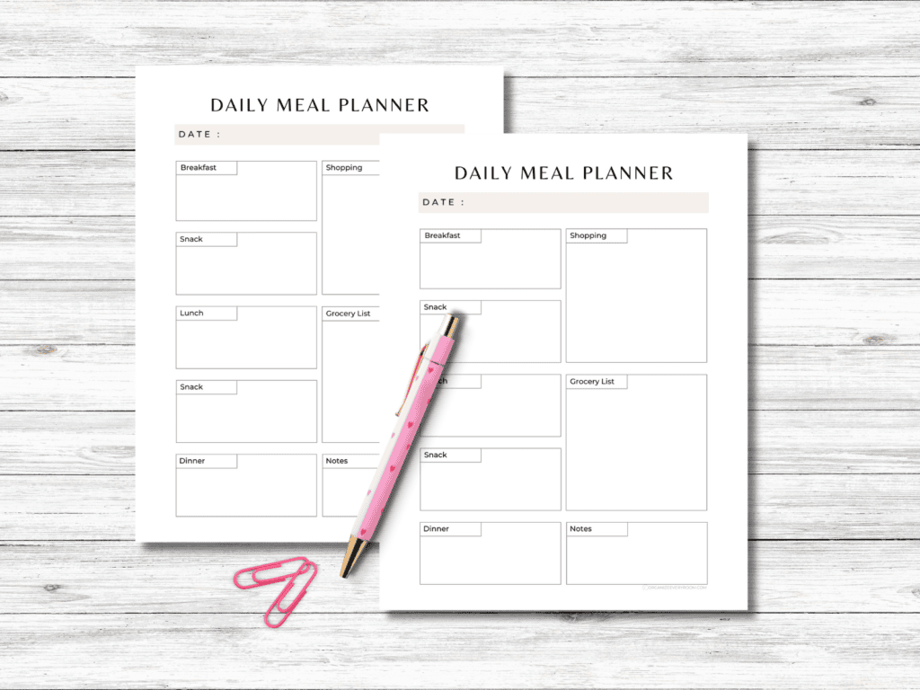 The daily meal planner pages on a desk with a pen and paper clips.