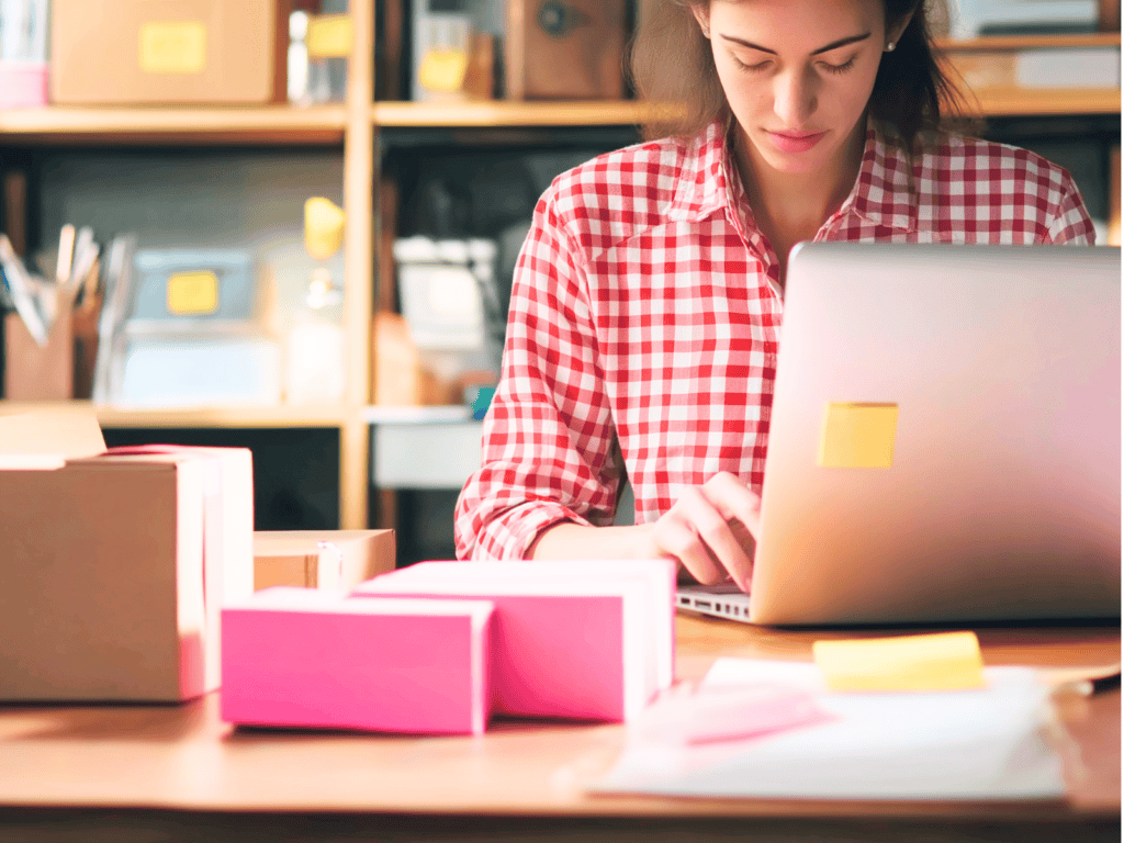 A woman looking at a laptop with boxes sitting on a table beside her.