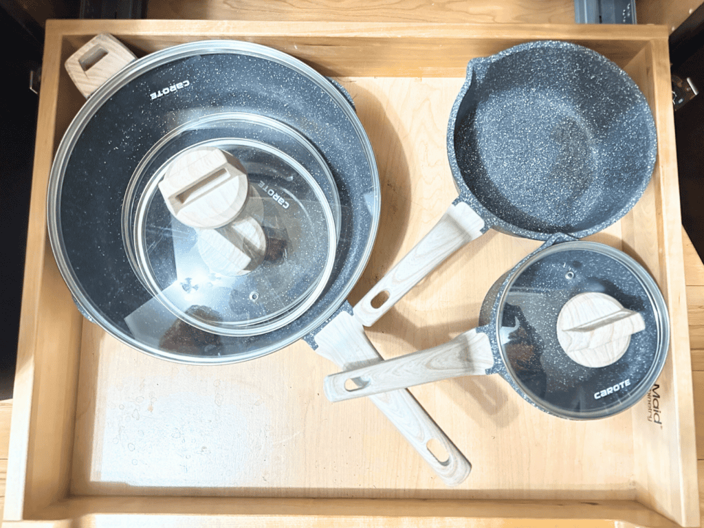 Three cook pans with glass lids in a kitchen cabinet.