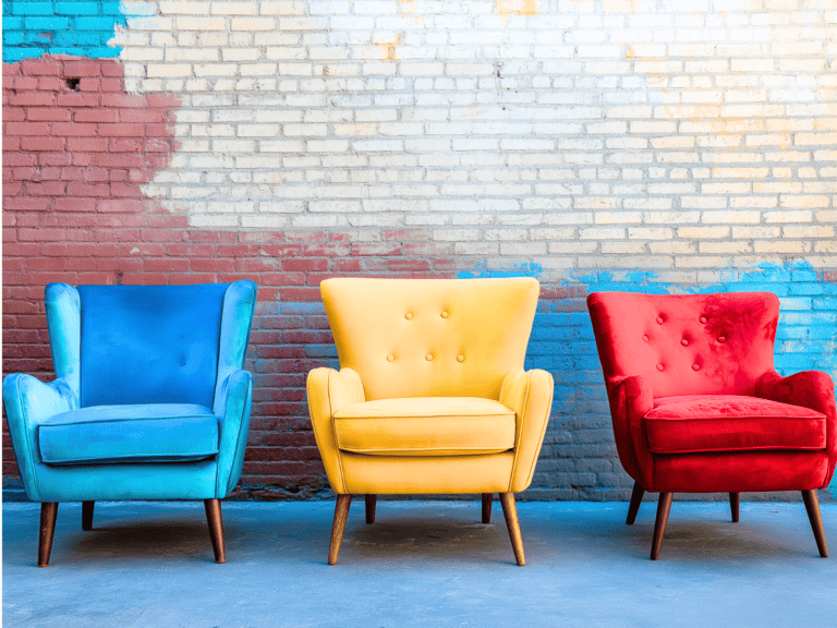 Three different color chairs sitting outside with a brick wall behind them.