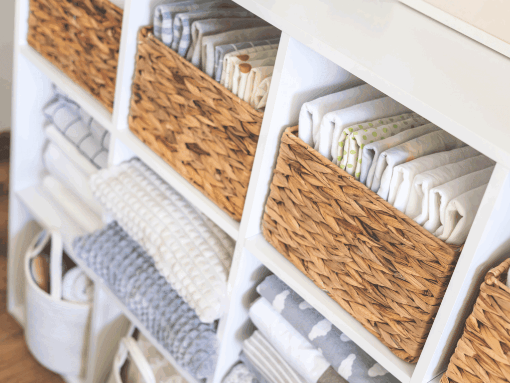 A close-up view of neatly organized white cubed shelves holding woven wicker baskets filled with folded fabrics and linens.