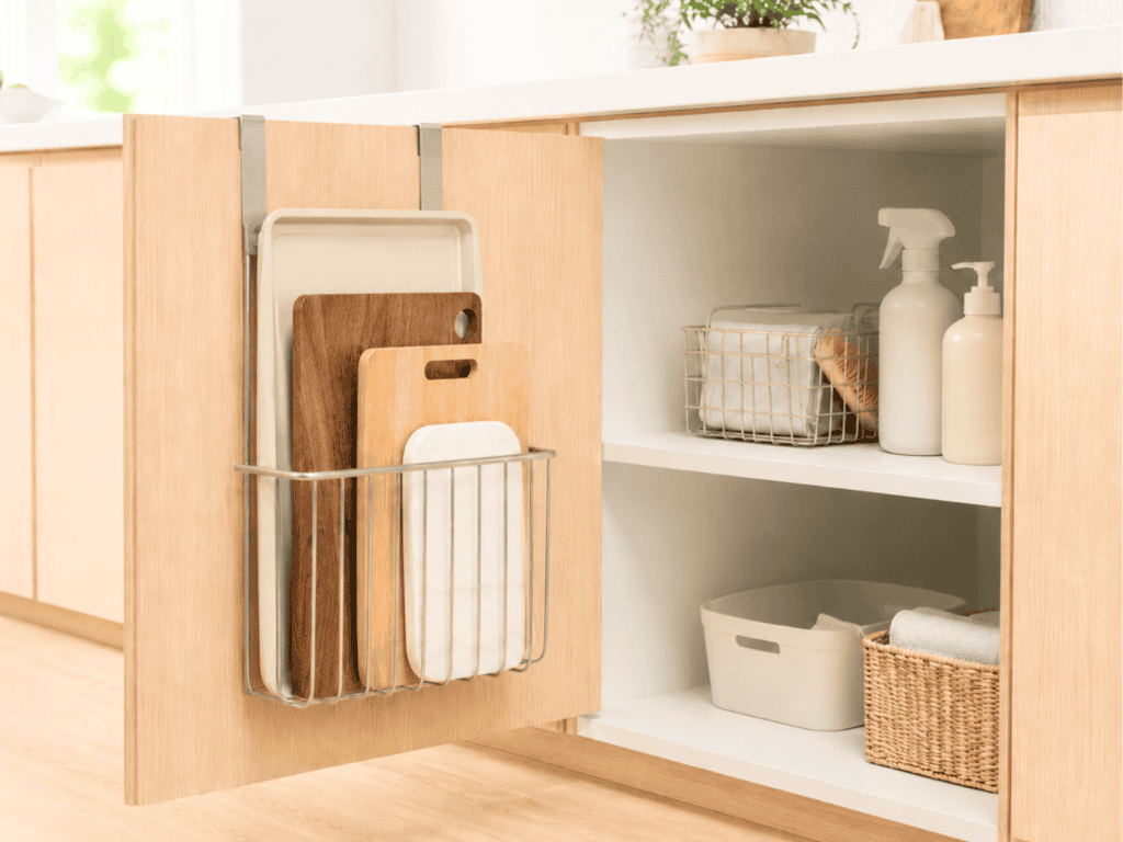 A kitchen cabinet door with an organizer hanging on it that contains cutting boards and cookie sheets.
