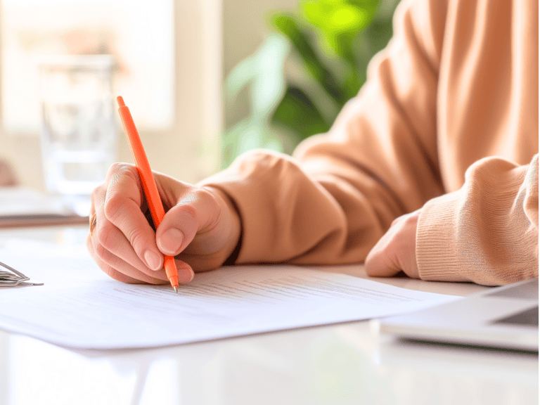 This close-up shot focuses on a person's hands as they write on a piece of paper with an orange pen, suggesting an engagement with organization lists.