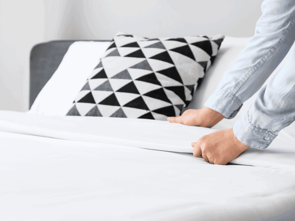 Hands making a bed with white bedding.