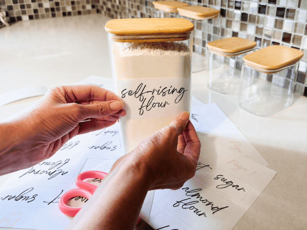 Hands putting a label on a glass container of flour.