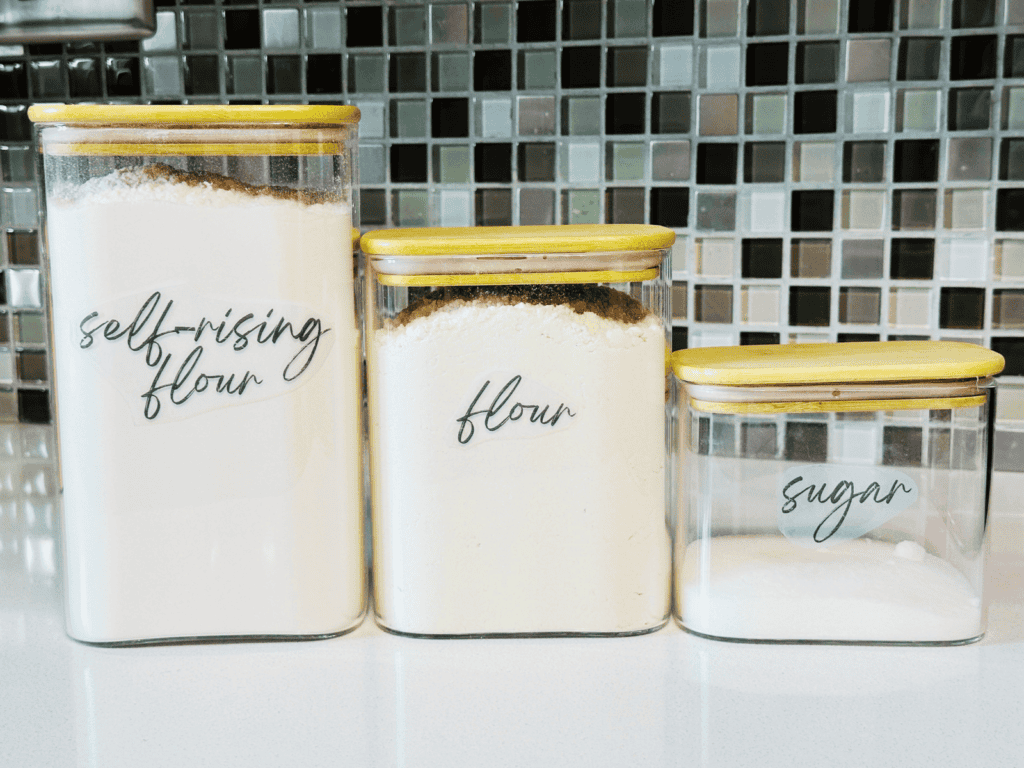 Three labeled pantry containers sitting on a kitchen countertop.