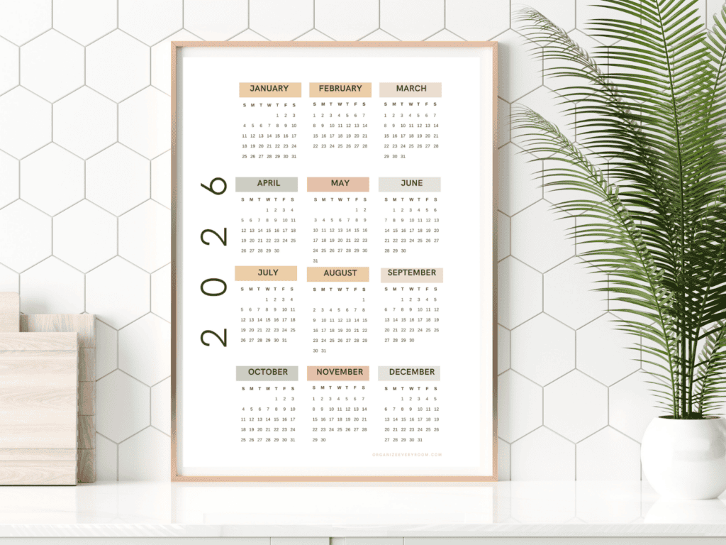 Minimalist framed 2026 yearly calendar printable showing all twelve months, styled on a shelf with modern decor and a green plant.