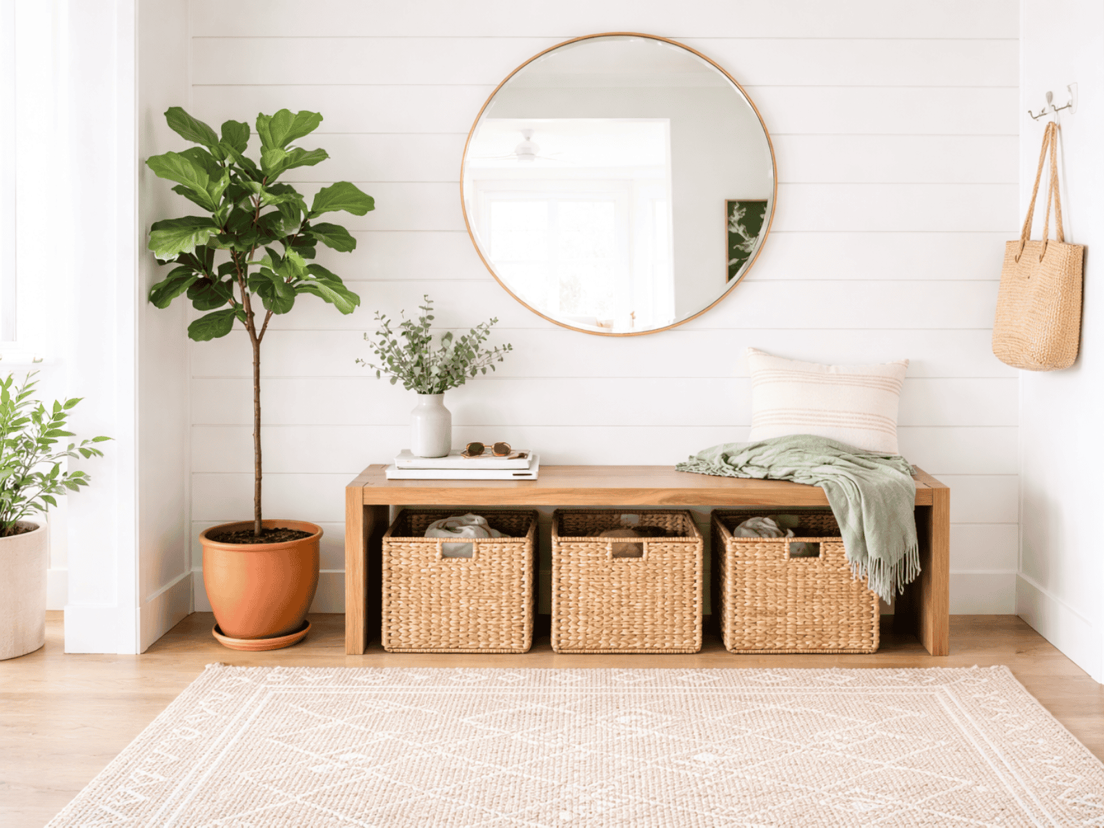 Bright, organized entryway with a wooden bench, woven storage baskets, and a round mirror, showing a calm and functional home system.