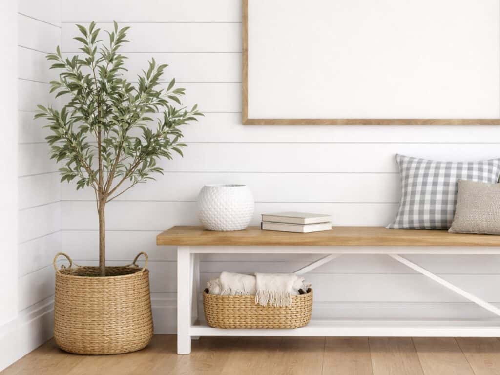 Minimalist entryway with wooden bench, decorative pillows, and potted plant against a white shiplap wall.