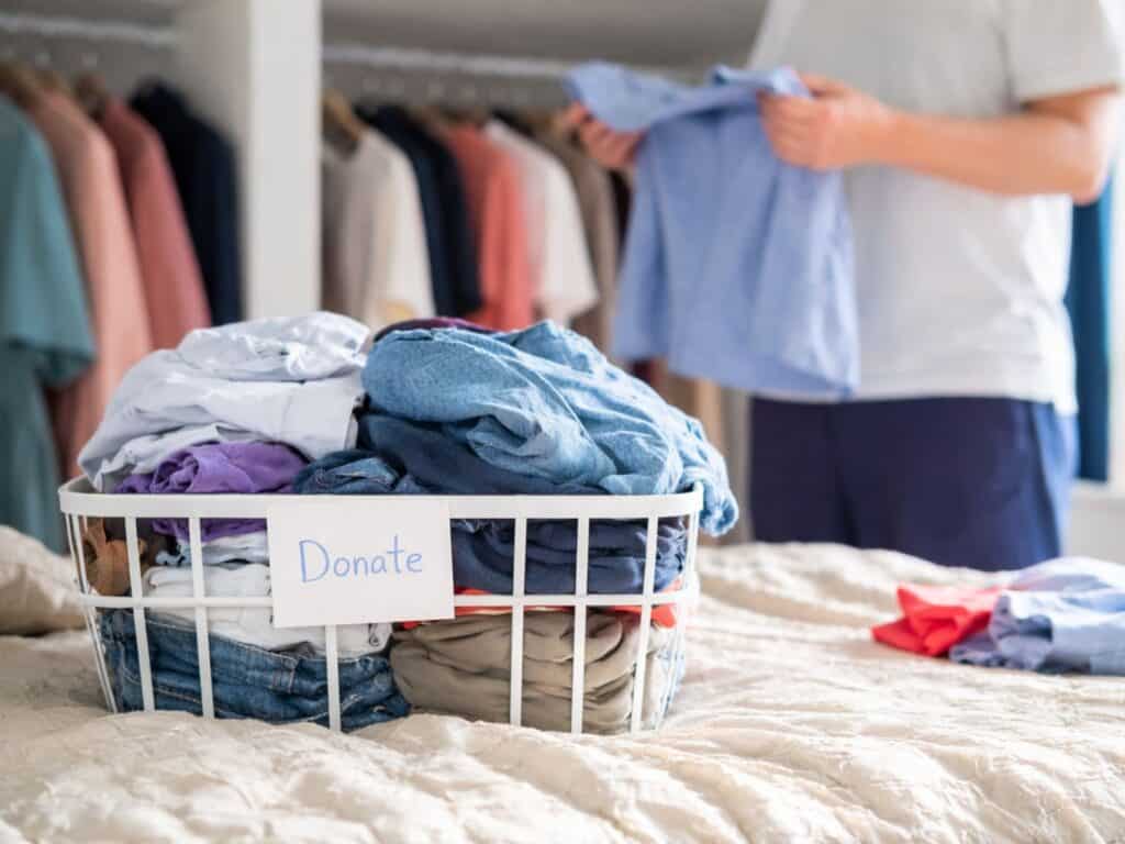 Clothes folded into a donation basket while organizing a closet in a bright bedroom